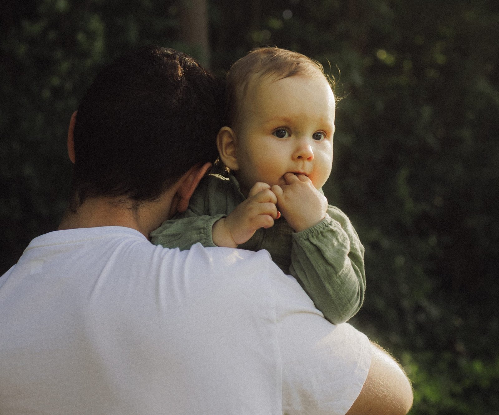 A father carrying his baby son on his shoulder through sunlit woodland, the boy looking back at the camera