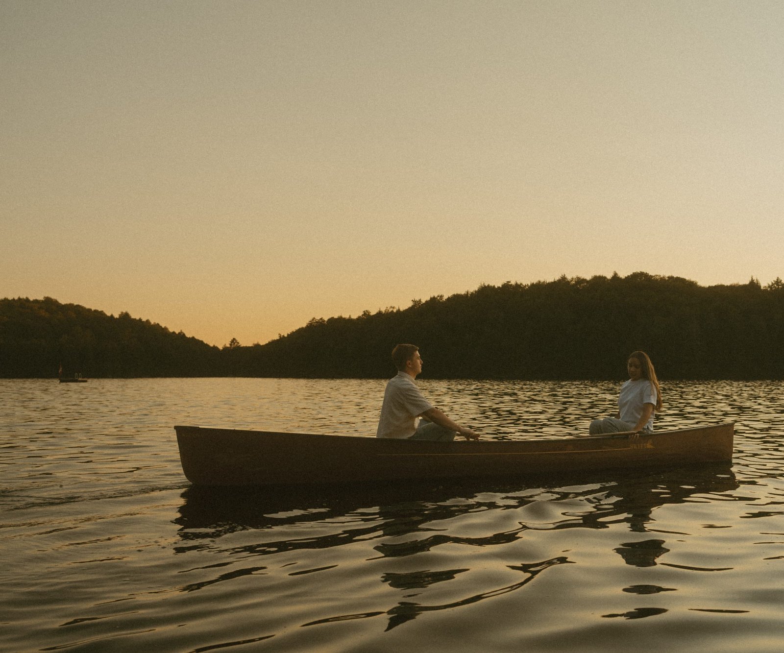 A couple sitting together in a canoe at sunset on a still lake